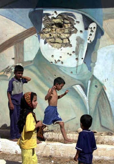 
The defaced image of former Iraqi President Saddam Hussein hangs on a Baghdad monument where children play. Legal custody of Saddam  and 11 others was transferred to the Iraqis on Wednesday. 
 (Associated Press / The Spokesman-Review)