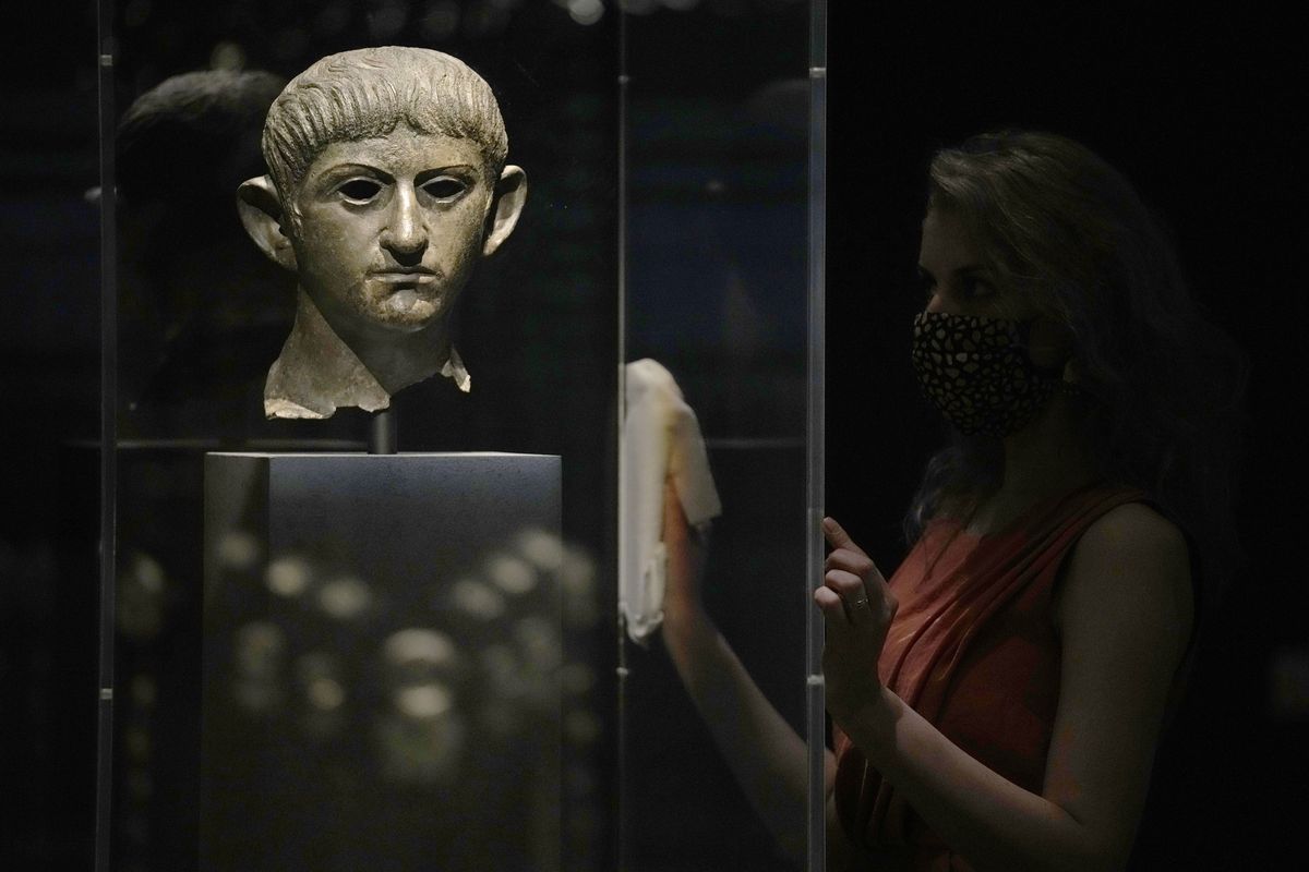 A museum employee poses for photographers next to a bronze head of Roman emperor Nero dating from around AD 54-61 and found in the River Alde at Rendham in Suffolk, eastern England, during a media preview for the "Nero: the man behind the myth" exhibition, at the British Museum in London, Monday, May 24, 2021. The exhibition, which opens to visitors on May 27 and runs until October 24, explores the true story of Rome