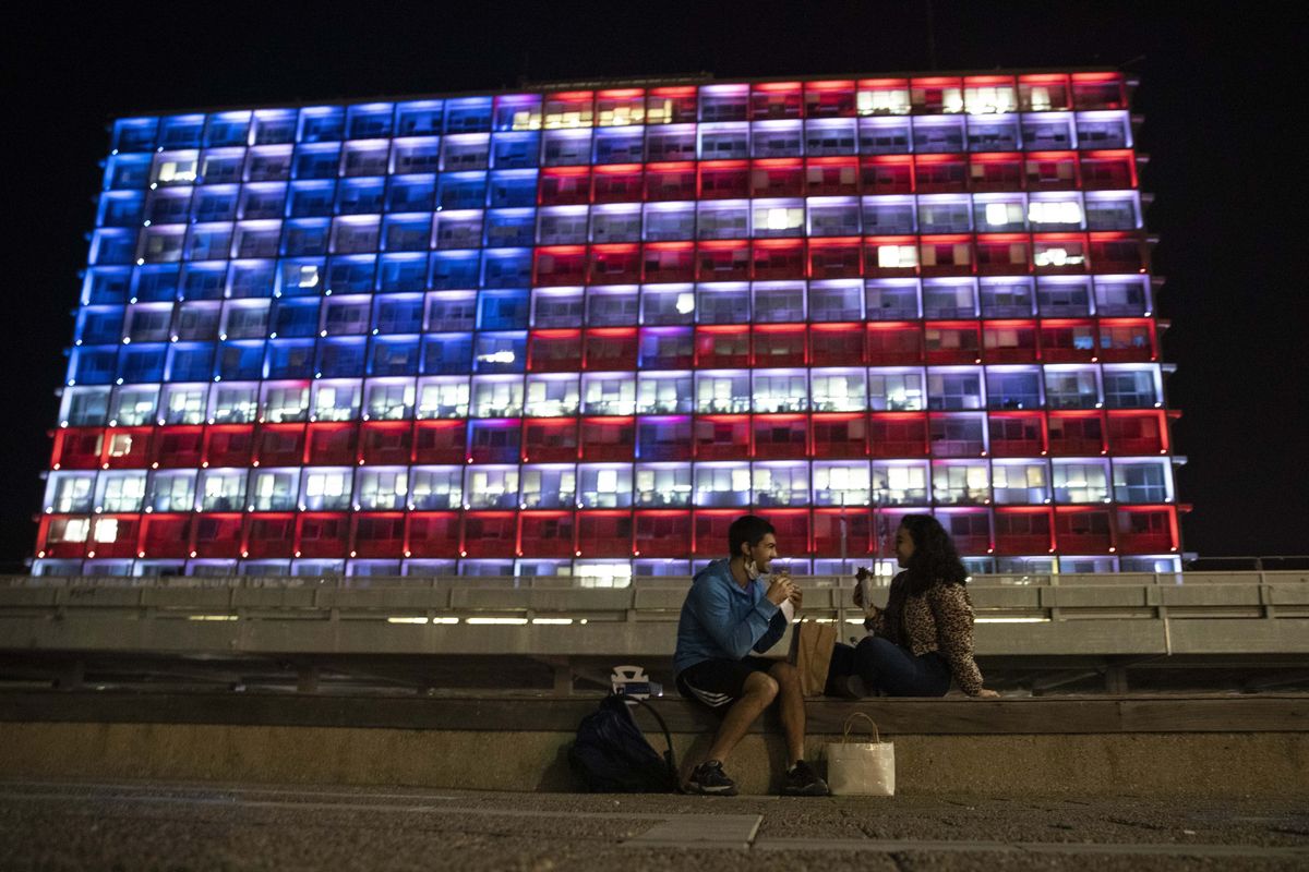 An Israeli couple sits near the Tel Aviv municipality building as it is lit up with the flag of the United States in Tel Aviv, Israel, Thursday, Jan. 7, 2021. Officials said the display is a sign of solidarity with the United States and support for democracy.  (Sebastian Scheiner)