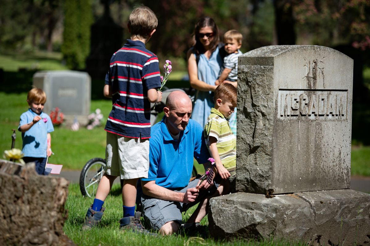 The Rose family – 3-year-old Thomas, left, 11-year-old Joseph, father Matt, mother Shaunna, 1-year-old Henry and 6-year-old Noah – lays flowers at a headstone Sunday for Memorial Day at Heritage Funeral and Cremation. The family also brought American flags to plant, and the boys stopped at multiple gravestones to clear debris on the way to visit other graves.  (Libby Kamrowski/ THE SPOKESMAN-REVIEW)