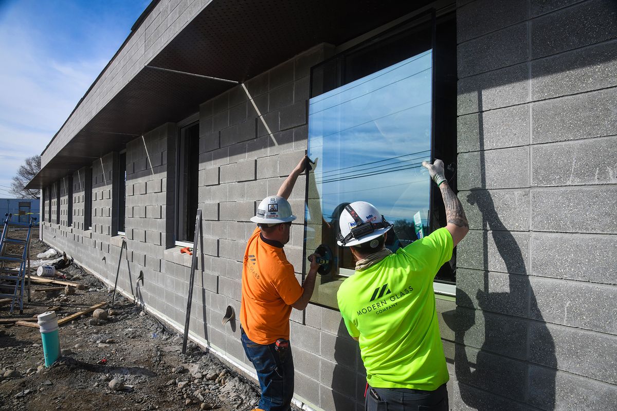 Taylor Tompkins, left, and Trevor Makinson, of Modern Glass install a window on the Spokane Public School side of the The Hive building, Thursday, March 4, 2021, in Spokane. The other side of the building is for Spokane Public Library.  (Dan Pelle/The Spokesman-Review)