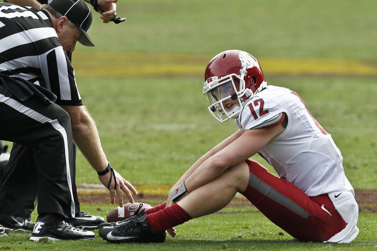 WSU quarterback Connor Halliday sits on the turf after being sacked as umpire Rick DiBernardo reaches in to pick up the ball. (Associated Press)