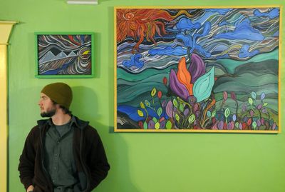 Artist Max Brown with his abstract paintings, “Egyptian Sun” and “Quest for the Top,” at his home in north Spokane. (Dan Pelle / The Spokesman-Review)