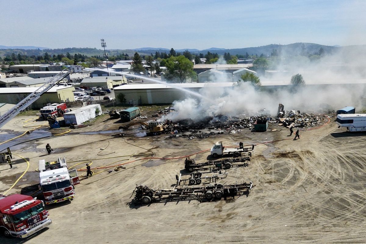 Spokane area firefighters dump water on a pile of smoldering debris at Evergreeen State Towing Monday, May 4, 2026 near Francis Avenue and Perry Street in North Spokane. The business dismantles unwanted recreational vehicles and the pile was likely associated with that process.  (Jesse Tinsley/THE SPOKESMAN-REVI)