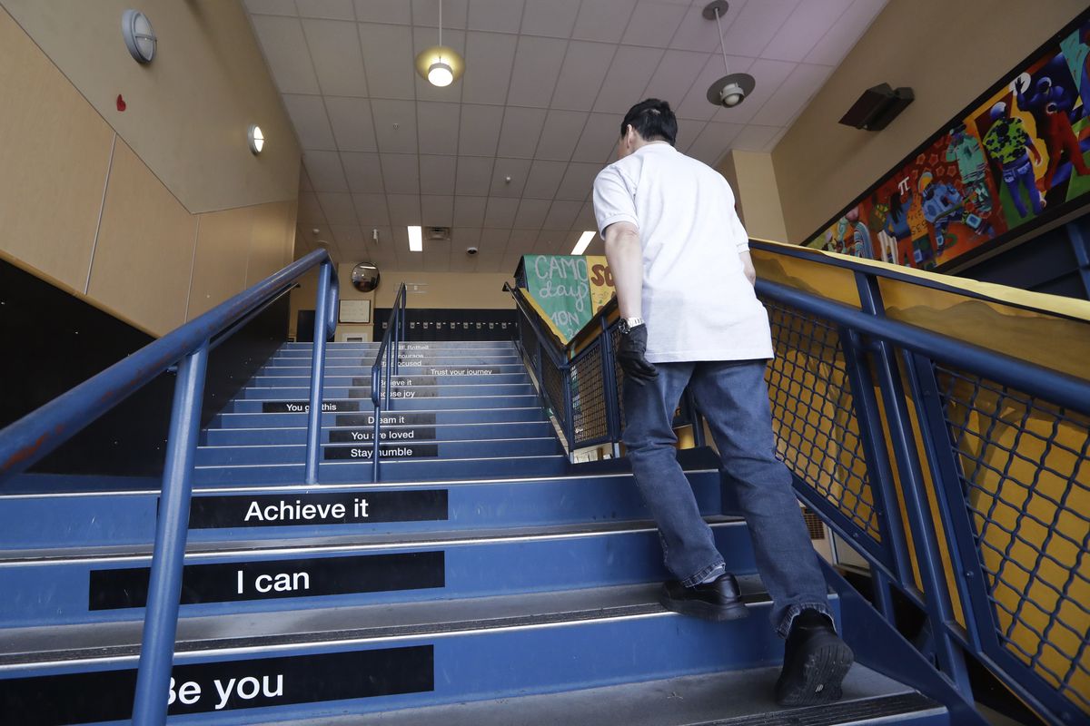 A school janitor walks up stairs inside Bothell High School, closed for the day, Thursday, Feb. 27, 2020, in Bothell, Wash. The suburban Seattle school was closed Feb. 27, after a staffer's family member was placed in quarantine for showing symptoms of possibly contracting the new virus. The school was cleaned and disinfected while students stayed home. On Friday, Oct. 24, the Seattle Public Schools announced the remote learning model would continue for the rest of the current semester because of an increase in COVID-19 cases in King  County.  (Elaine Thompson)