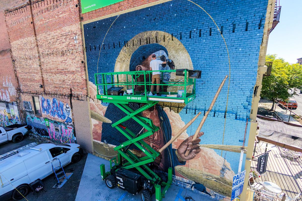 Artist Miles Toland works on a scissor lift while painting a large mural Monday featuring the image of musician Quindrey Davis on the side of the Longbotham Building on Main Avenue in downtown Spokane. The popular drummer and music teacher died of leukemia in 2023.  (Jesse Tinsley/THE SPOKESMAN-REVIEW)