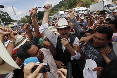 Ousted Honduras President Manuel Zelaya, surrounded by supporters and the press, lifts the chain that marks the border between Nicaragua and Honduras in Las Manos, Nicaragua, on Friday.  (Associated Press / The Spokesman-Review)