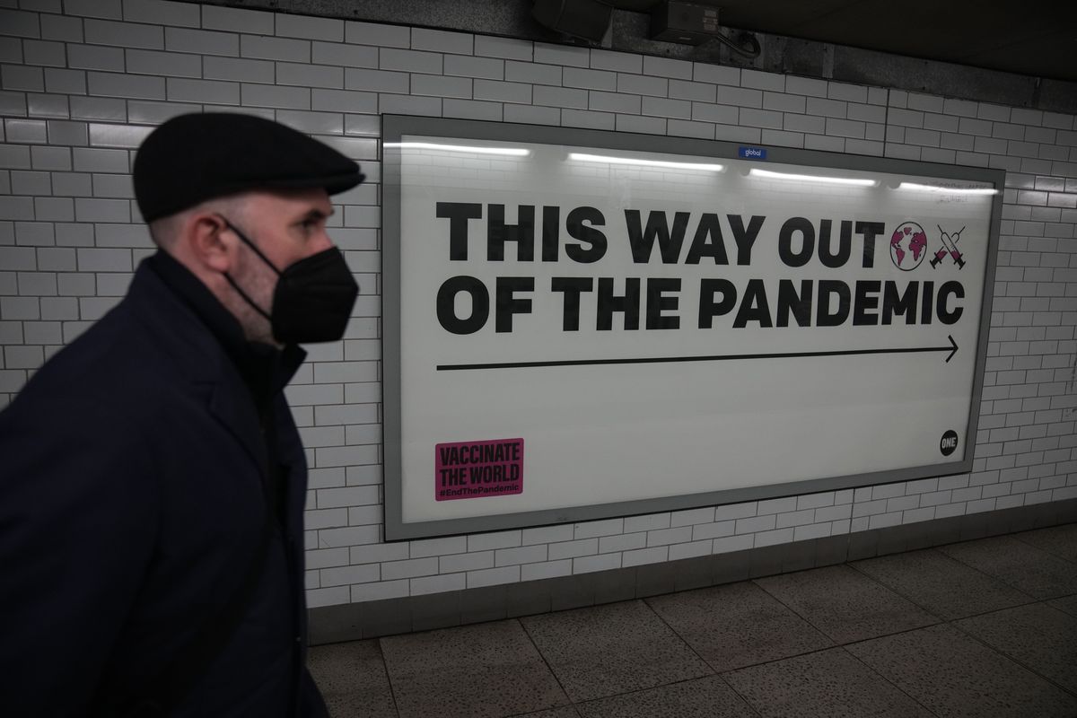 A man wearing a face mask to curb the spread of coronavirus walks past a health campaign poster from the One NGO, in an underpass leading to Westminster underground train station, in London, Thursday, Jan. 27, 2022. Most coronavirus restrictions including mandatory face masks were lifted in England on Thursday, after Britain