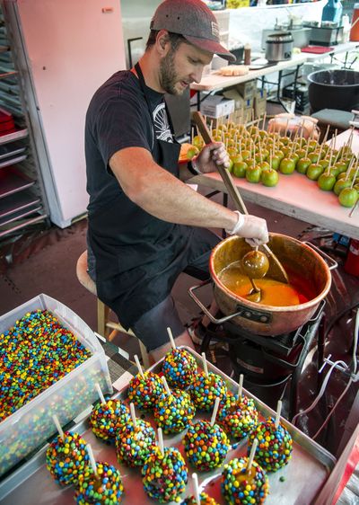 Sticking point: Shawn Taranto dips Granny Smith apples in caramel, then rolls them in M&M chocolate candies in the Charlie’s Cheesecakes food booth at Pig Out in the Park on Friday in Riverfront Park. The 34th-annual food, drink and concert festival, featuring 47 food booths, four adult beverage gardens and 100 free concerts on four stages, is open from 10 a.m.-10 p.m. through Labor Day. (Colin Mulvany)