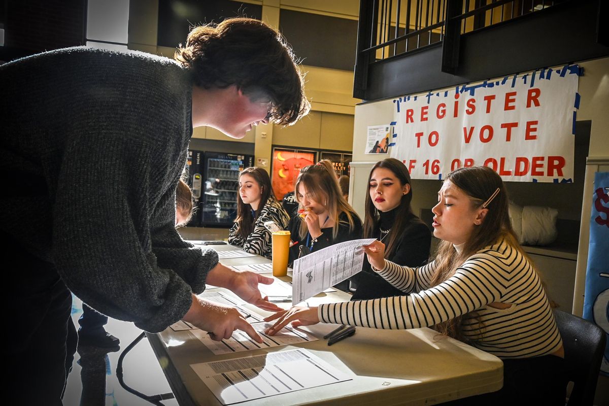 Ukrainian student Anna Dubova, right, hands West Valley High School junior Henry Sinclair, 16, a voting registration form on Tuesday in the school’s cafeteria. Also at the table, from left, are Kateryna Bauer, Antonina Bohouyk and Viktoriya Aparina.  (Dan Pelle/THE SPOKESMAN-REVIEW)
