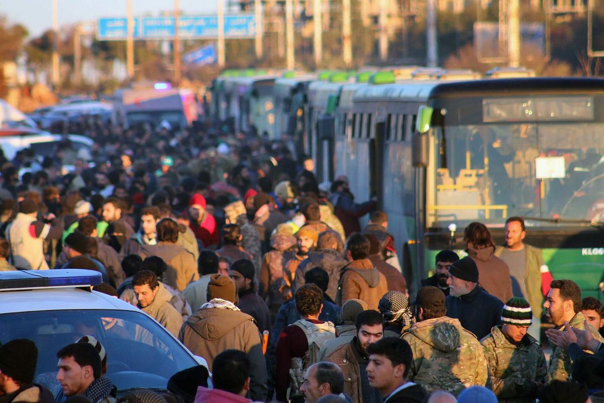 This image released on Thursday, Dec. 15, 2016, by Aleppo 24, shows residents gathered near green government buses as they hold their belongings for evacuation from eastern Aleppo, Syria. (Uncredited / Associated Press)