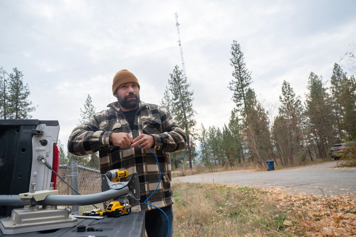 Christopher Carson, left, of Sp’q’n’i Broadband Services, prepares to install a wireless broadband antenna on a house just a stone’s throw from a tower (background) in the Westend community on the Spokane Reservation.  (Jesse Tinsley/THE SPOKESMAN-REVI)