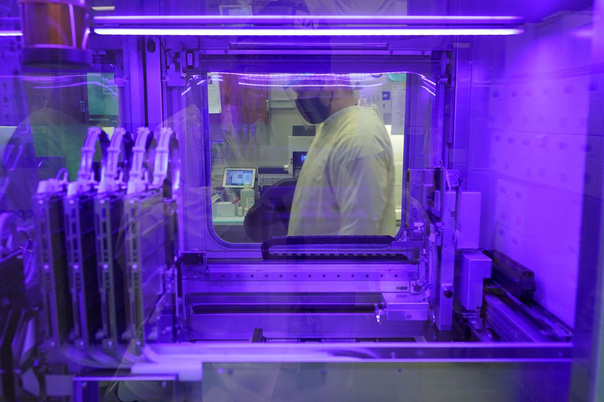 Steven Grimmett, a microbiologist on the COVID-19 team at the Washington State Department of Health’s Public Health Laboratory, is seen through a window of a machine that identifies positive and negative COVID-19 cases on Dec. 7 in Shoreline, Wash.  (Ted S. Warren)