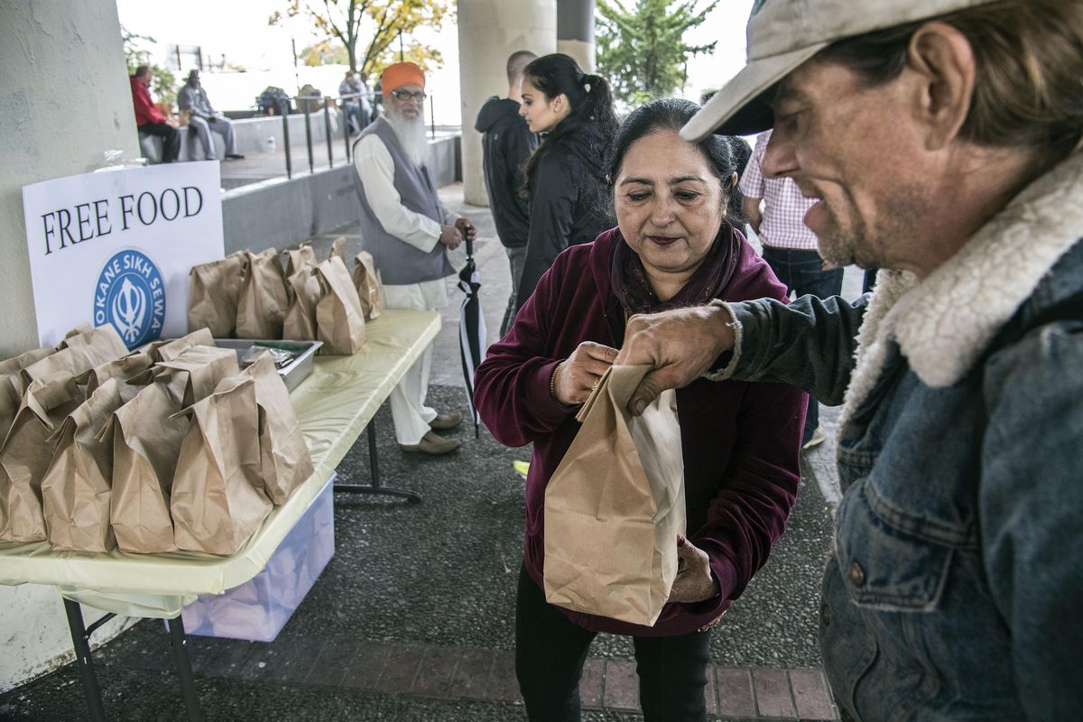 Amarjit Kuar offers a lunch bag with a peanut butter and jelly sandwich to Ray Kalebaugh, Sept. 17, 2016, under the freeway at Fourth Avenue and McClellan Street in downtown Spokane, Wash. Members of the Sikh Temple of Spokane prepared and distributed 150 lunches for the homeless. (Dan Pelle / The Spokesman-Review)