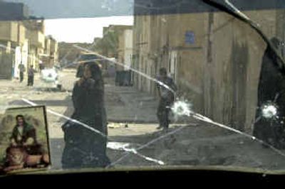 
Iraqis pass by a shattered window of a car in the Baghdad suburb of Al Sadr City on Sunday. 
 (Associated Press / The Spokesman-Review)