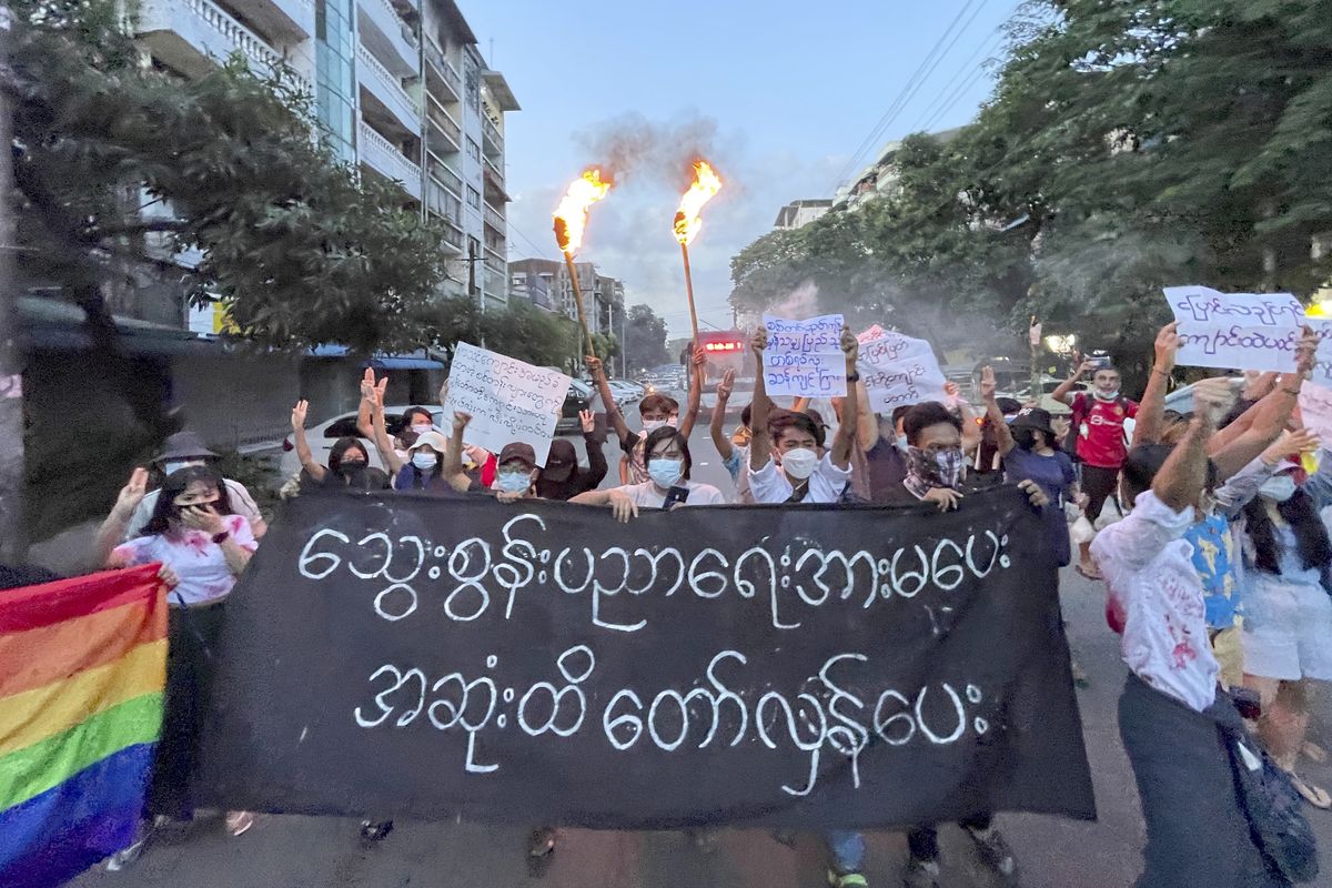 A small group of protesters hold a banner which reads in Burmese 
