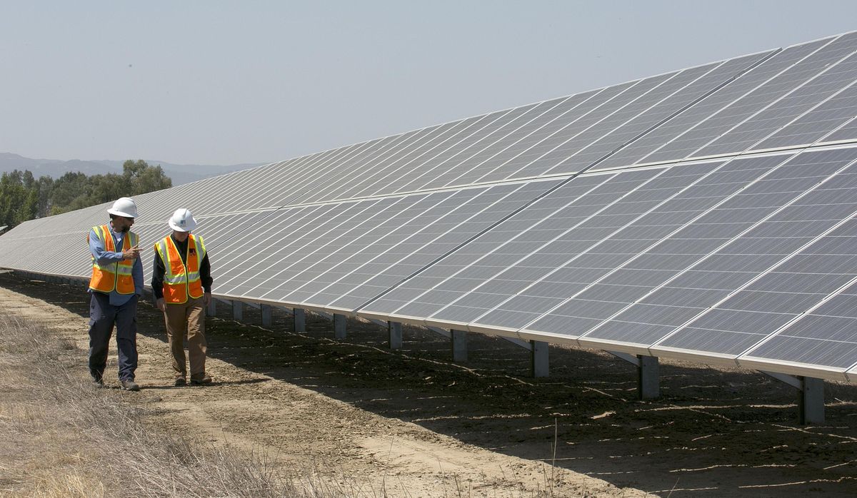 FILE - In this Aug. 17, 2017 photo, solar tech Joshua Valdez, left, and senior plant manager Tim Wisdom walk past solar panels at a Pacific Gas and Electric Solar Plant, in Dixon, Calif. Cheap solar panels imported from China and other countries have led to a boom in the U.S. solar industry, where rooftop and other installations have surged 10-fold since 2011. But two U.S. solar manufacturing companies say the flood of imports has led one to bankruptcy and forced the other to lay off three-quarters of its workforce. (Rich Pedroncelli / Associated Press)