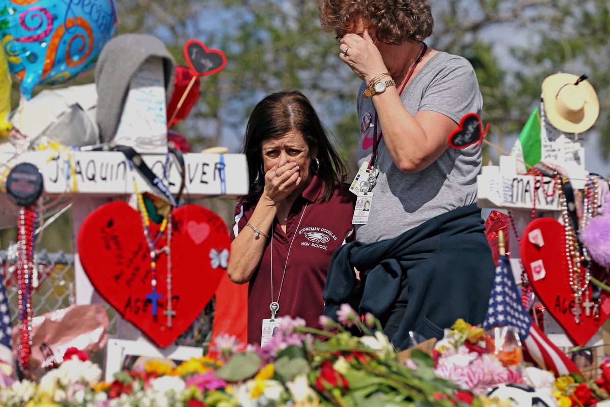 FILE - Marjory Stoneman Douglas High School administrative employees Margarita LaSalle, left, and JoEllen Berman, walk along the hill near the school lined with 17 crosses to honor the students and teachers killed on Valentine