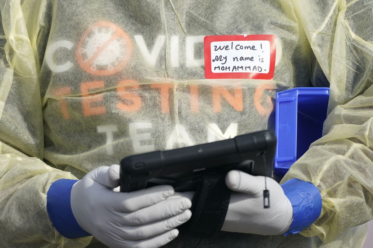 FILE - In this Oct. 28, 2020, file photo, a worker wearing gloves, and other PPE holds a tablet computer as he waits to check people at a King County coronavirus testing site in Auburn, Wash., south of Seattle. The latest surge in U.S. coronavirus cases appears to be larger and more widespread than the two previous ones, and it is all but certain to get worse. But experts say there are also reasons to think the nation is better able to deal with the virus than before, with the availability of better treatments, wider testing and perhaps greater political will.  (Ted S. Warren)