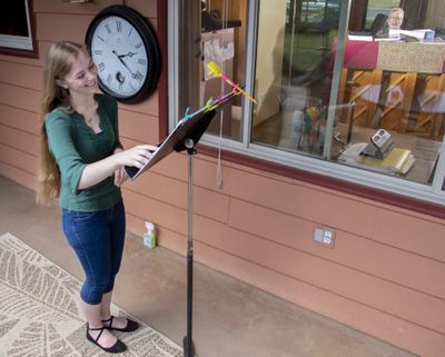 Voice teacher Nancy Klingman, right, sits at an upright piano inside her Spokane home and gives a voice lesson while voice student Maleny Mannino stays on the back patio and sings Tuesday.  (JESSE TINSLEY/The Spokesman-Review)