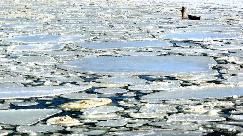 In this photo taken on Feb. 18, 2010,  a fisherman stands near his boat  on the main channel of the Mississippi River as ice begins to break apart from warmer temperatures near Dubuque, Iowa. (Dave Kettering / Telegraph Herald)