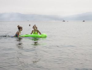 Kaylah and Kiara Ukrainetz of Edmonton, Alberta swim on an inflatable Wednesday in Lake Coeur d’Alene. Hazy skies are due to a high volume of smoke in the air, and multiple public agencies are advising people to stay indoors as much as possible due to poor air quality. (Jake Parrish / Coeur d'Alene Press)