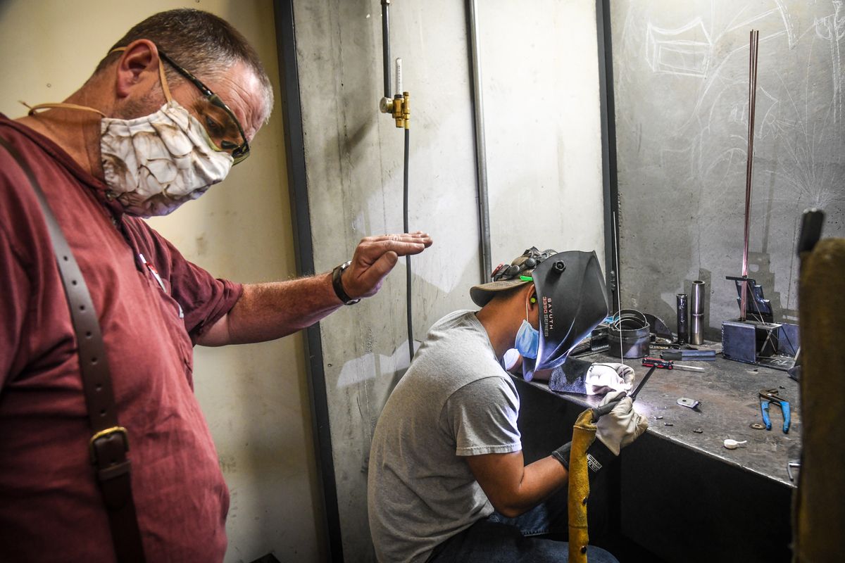 Spokane Community College welding instructor Jeff Schwab, left, shields his eyes as student Savuth Vann welds during class on Thursday, July 23, 2020. SCC students and instructors have returned to in-person classes but are taking steps to curb the spread of the novel coronavirus, including wearing masks and socially distancing.  (Dan Pelle / The Spokesman-Review)