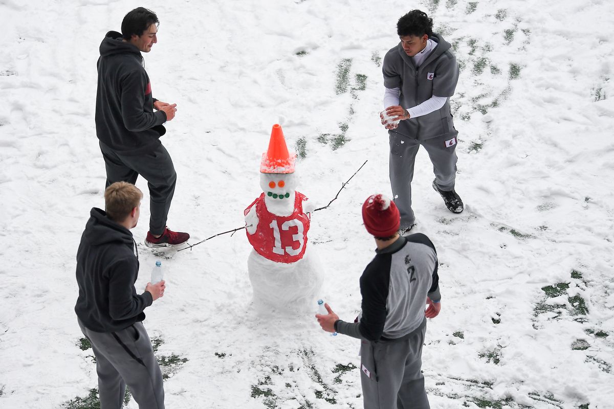 Washington State Cougars quarterbacks Gunner Cruz (15), upper left, Jayden de Laura (4), upper right, and Cammon Cooper (2), lower right, discuss the finishing touches for an impromptu snowman they built with teammates following the cancellation of WSU