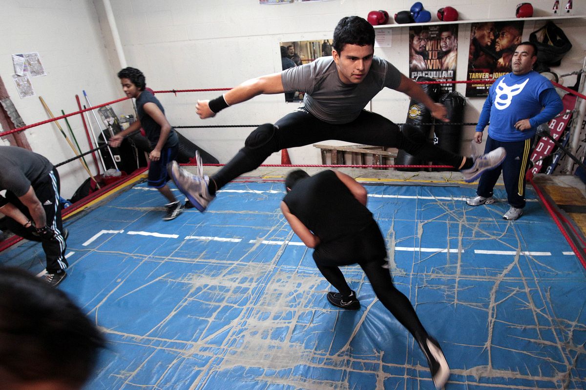 Lucha Libre Volcánica coach Jose Gomez, right, watches as David Gonzalez leaps over a teammate as they practice lucha libre, Mexico’s style of wrestling, in a garage-turned-boxing gym in Renton, Wash. (Associated Press)