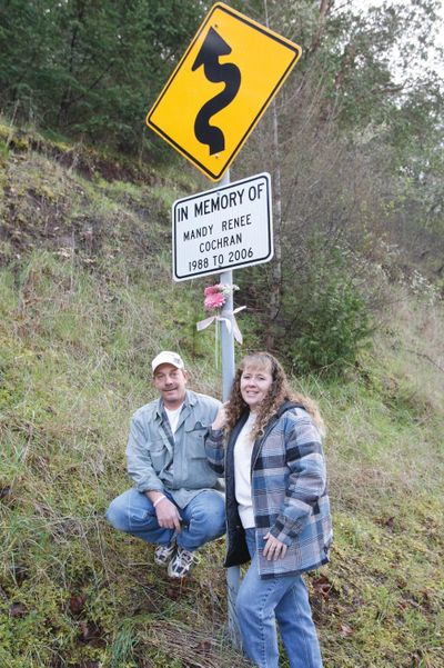 Shane Hutchison and his wife, Dawn Hutchison, stand with a sign alerting drivers to  upcoming curves in Roseburg, Ore., last month. The couple’s daughter Mandy Cochran was killed in an accident on the narrow road.  (Associated Press)