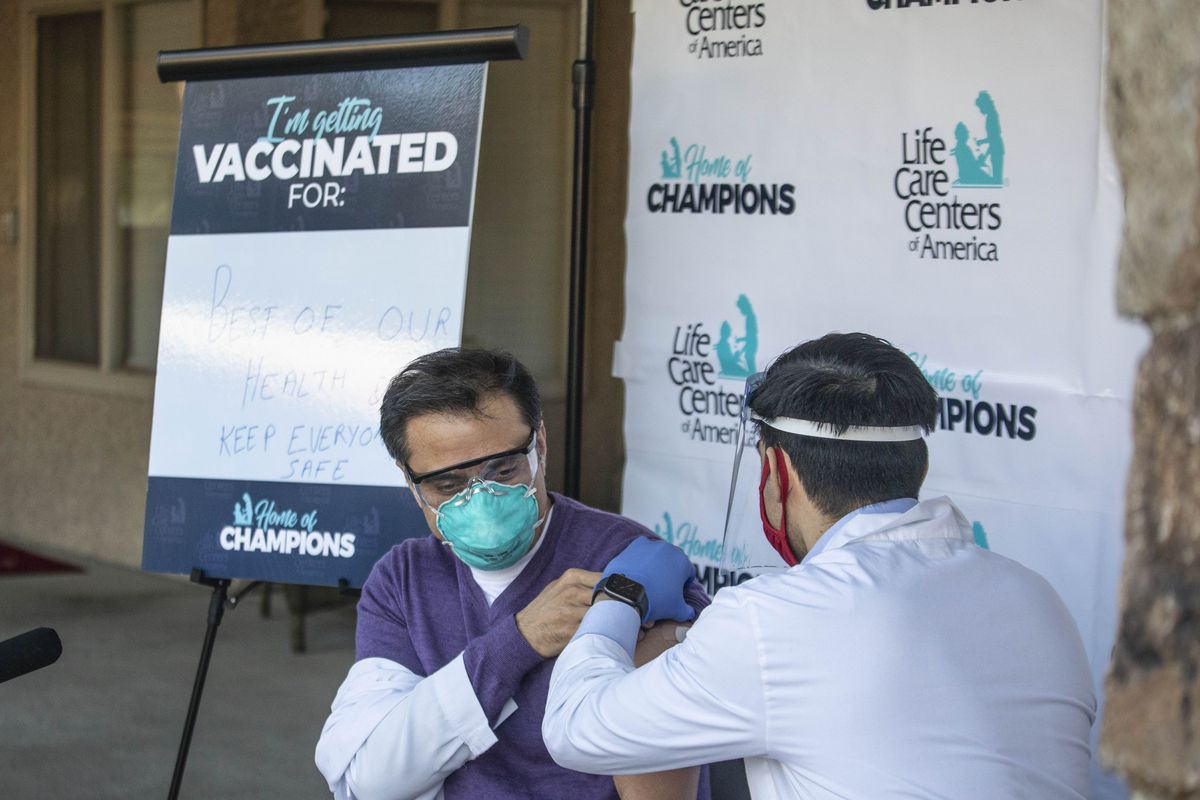Dr. Dhirendra Kumar, Medical Director, and Attending Physician at Life Care Center in Kirkland is vaccinated by Matt Talavera, a pharmacist for CVS outside the Center in Kirkland, Wash., Monday, Dec. 28, 2020.  (Steve Ringman)