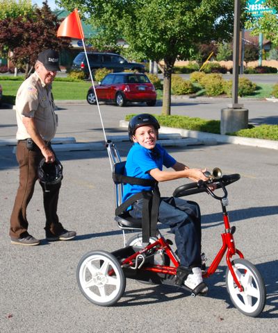 Trayton Larsen, 11, zips around outside  the Spokane Valley Police Department, where SCOPE volunteers and his grandfather gave him a custom- made three- wheeler. Al Fisher, background, organized fundraising for the gift. (John  Craig / The Spokesman-Review)