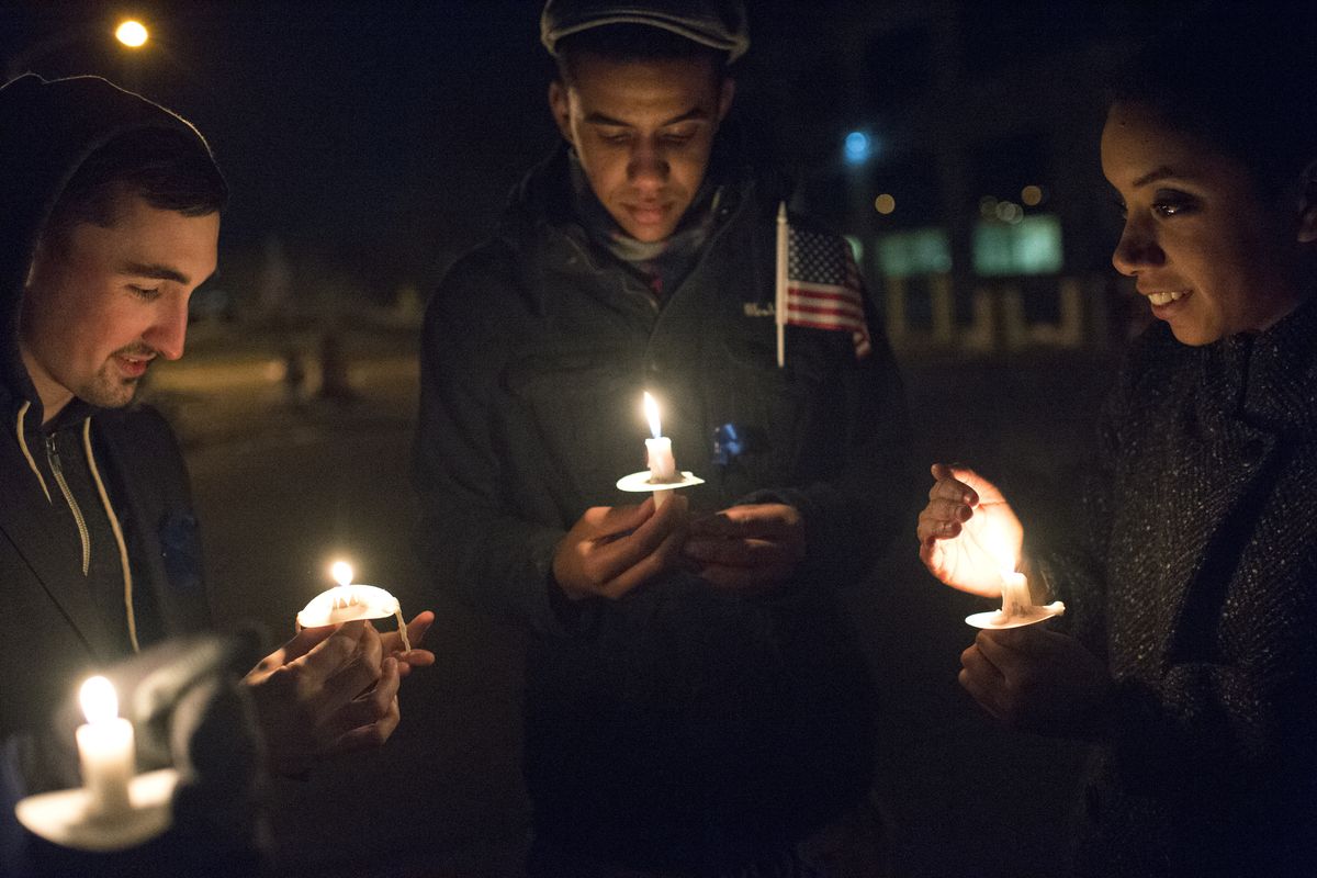 Shanice Applewhaite, right, smiles as she and her brother Kenny, center, join Erik Oberbarnsheidt in holding candles during a rally to support local law enforcement Friday at the Spokane Public Saftey Building in Spokane. The Applewhaites’ father is an officer with the Spokane Police Department. (Tyler Tjomsland)
