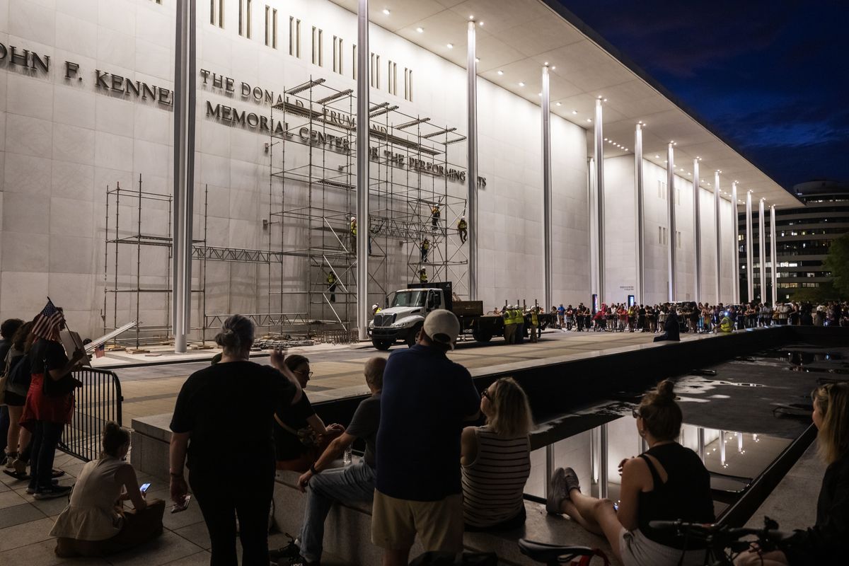 Spectators watch as workers put up scaffolding ahead of a court-mandated deadline to remove President Donald Trump