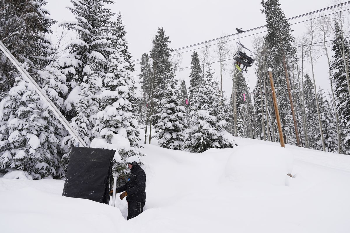 Ian Sidwell adjusts a machine used to make snow at Vail Mountain Resort as snowboarders ride a lift, Wednesday, Dec. 29, 2021, in Vail, Colo. Newer snowmaking technology is allowing ski areas to be more efficient with energy and water usage as climate change continues to threaten snowpack levels.  (Brittany Peterson)