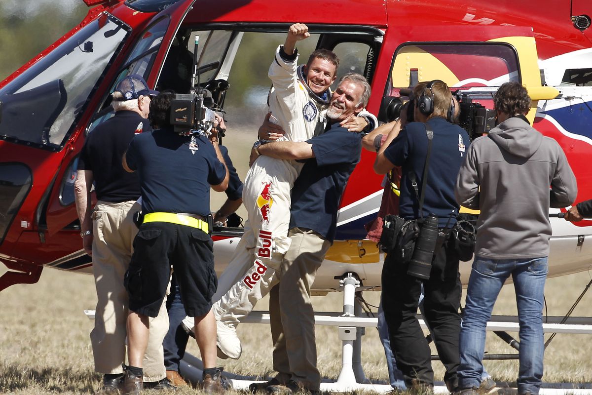 Felix Baumgartner, third from left, of Austria, gets a hug from Mission Control technical project director Art Thompson, as television crews and pool photographers converge on the scene, after Baumgartner successfully jumped from a space capsule lifted by a helium balloon at a height of just over 128,000 feet above the Earth