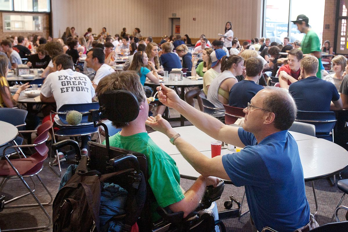 In a photo taken Tuesday, April 24, 2012, Steve Sutherland feeds his son, Ryan Sutherland, who has Duchenne muscular dystrophy, in the crowded dining room at Whitworth University in Spokane. The father and son, from Cashmere, Wash., have been dorm roommates at Whitworth University since Ryan started there in 2009. Ryan graduated with bachelor