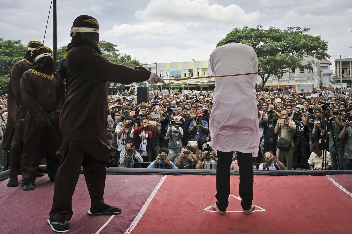Shariah law official whips one of two men convicted of gay sex during a public caning outside a mosque in Banda Aceh, Aceh province Indonesia, Tuesday, May 23, 2017. Two men in the province were publicly caned dozens of times Tuesday for consensual sex, a punishment that intensifies an anti-gay backlash and which rights advocates denounced as “medieval torture.” (Heri Juanda / AP)