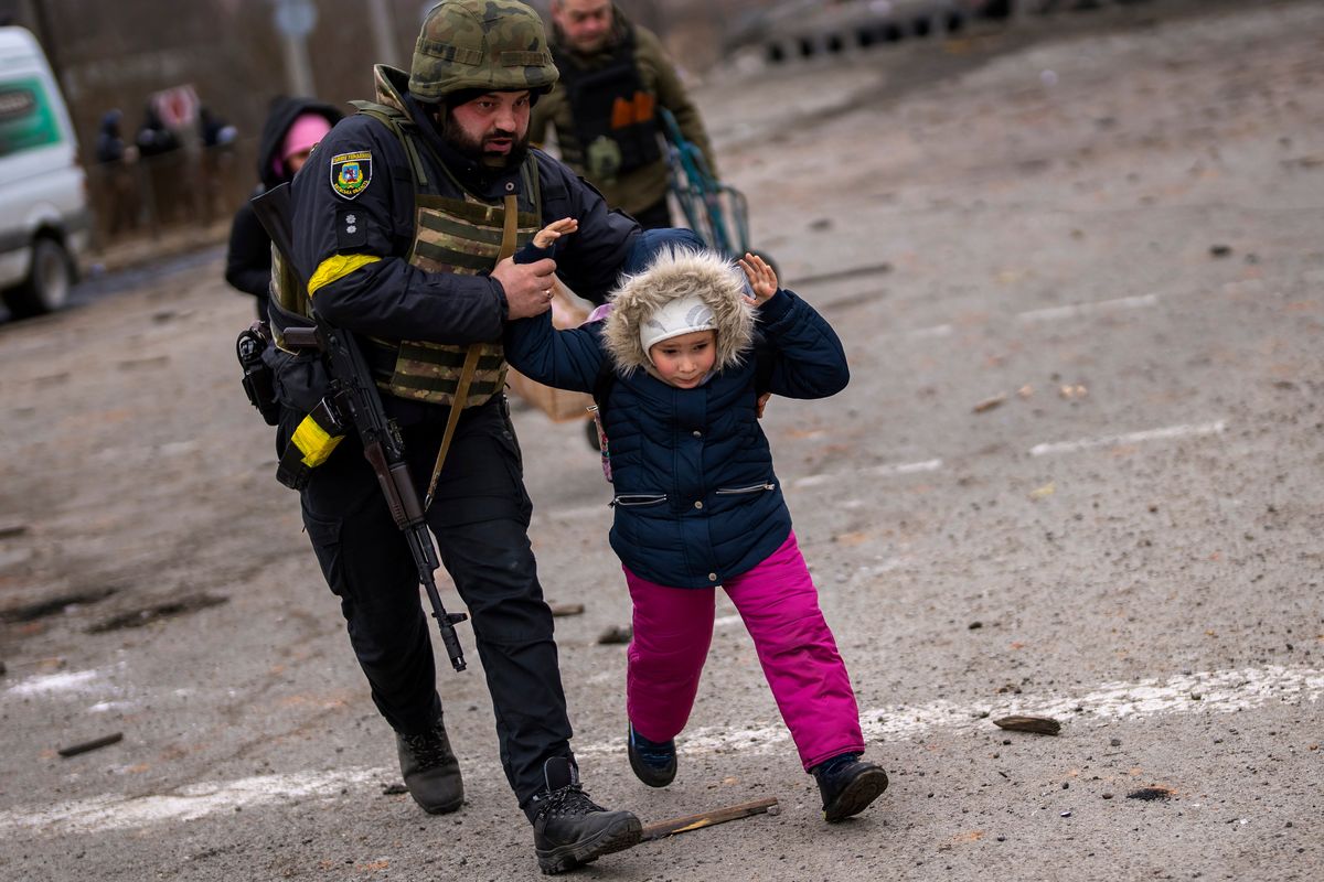 A Ukrainian police officer runs while holding a child as the artillery echoes nearby, while fleeing Irpin on the outskirts of Kyiv, Ukraine, on Monday.  (Emilio Morenatti)