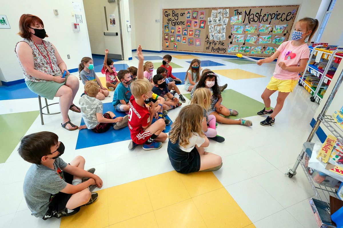 FILE — Kelly Sheridan, left, and her first grade students wear face masks as one of the students makes a presentation during class in a hallway at the Milton Elementary School, May 18, 2021, in Rye, N.Y. The New York State Education Department is telling schools to continue to require masks despite a judge’s ruling overturning the state