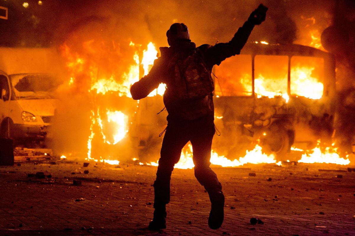 A protester throws a stone at a burning police bus in Kiev, Ukraine, on Sunday. Protesters clashed with riot police in the center of the Ukrainian capital. (Associated Press)