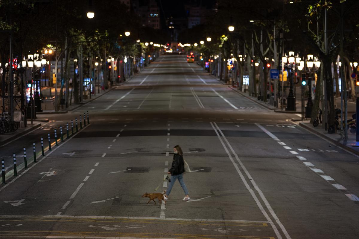 A resident walks with a dog on an empty street after curfew in Barcelona on Sunday, Oct. 25, 2020. Spain orders nationwide curfew to stem worsening outbreak. Spanish Prime Minister Pedro Sánchez has declared a second nationwide state of emergency in hopes of stemming a resurgence in coronavirus infections. (Emilio Morenatti)