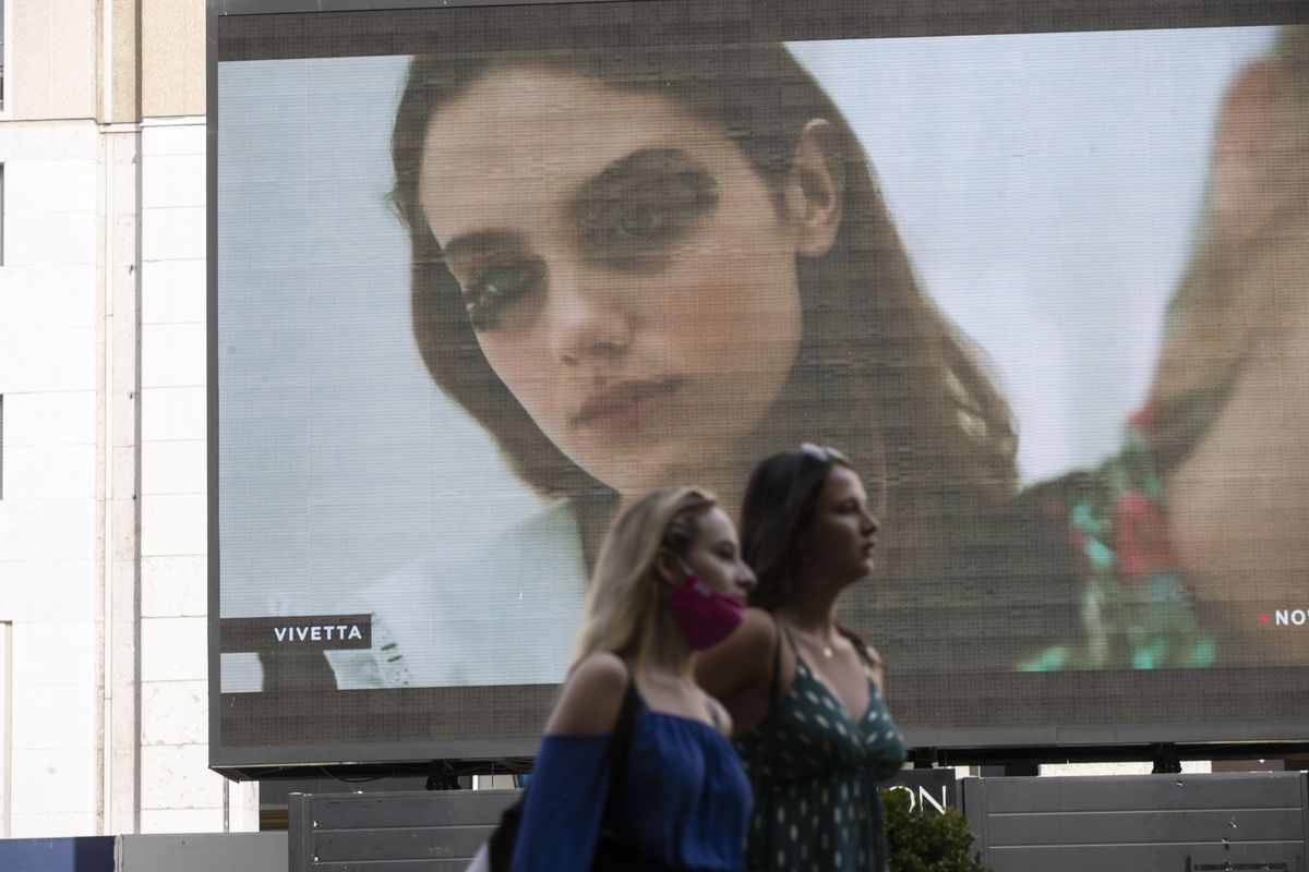 Pedestrians pass by a screen showing a Vivetta model during the Milan Digital Fashion Week, in Milan, Italy, Tuesday, July 14, 2020. Forty fashion houses are presenting previews of menswear looks for next spring and summer and pre-collections for women in digital formats, due to concerns generated by the COVID-19.  (Luca Bruno)