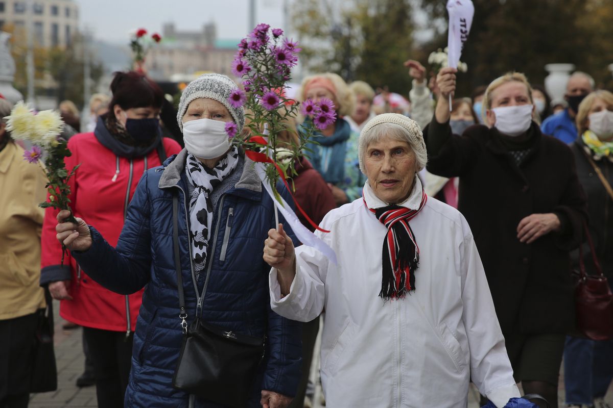 Elderly women hold flowers during an opposition rally to protest the official presidential election results in Minsk, Belarus, Monday, Oct. 12, 2020. Riot police clashed with protesting pensioners in central Minsk on Monday. The pensioners marched in a column through central Minsk, carrying flowers and posters with slogans such as "The grandmas are with you (protesters)." (STR)