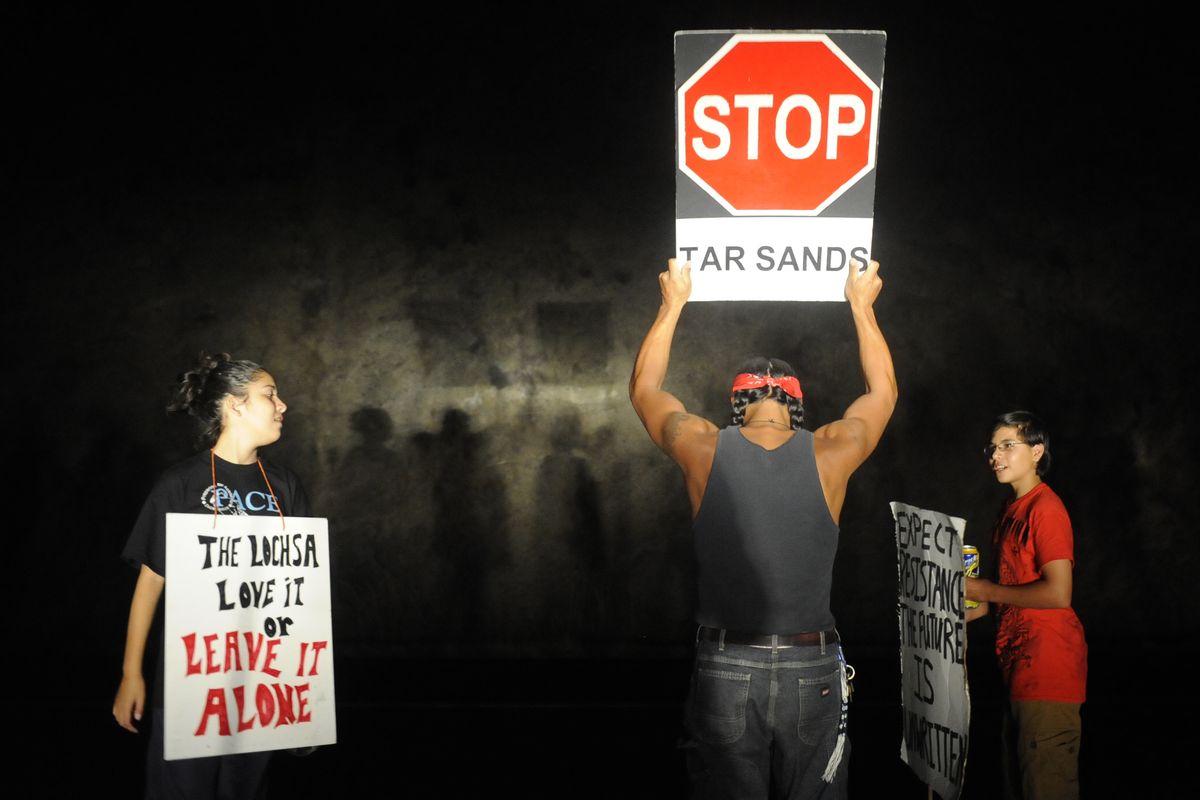 Brandon Metoxen, 24, a member of the Oneida Nation, center, is shown in headlights holding a sign protesting a megaload carrying an evaporator for a Canadian oil rig on Tuesday on U.S. Highway 12 outside of Lewiston. (Tyler Tjomsland)