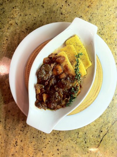 Lamb stew with butternut squash served over polenta and garnished with a sprig of thyme.