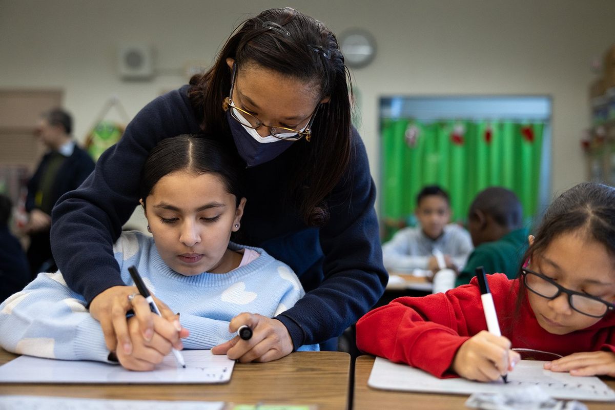 Tyara Brooks helps guide fourth-grade student Aaliyah Miranda-Garcia, left, and Sophia Ortega during a lesson on cursive writing.  (Christina House/Los Angeles Times)