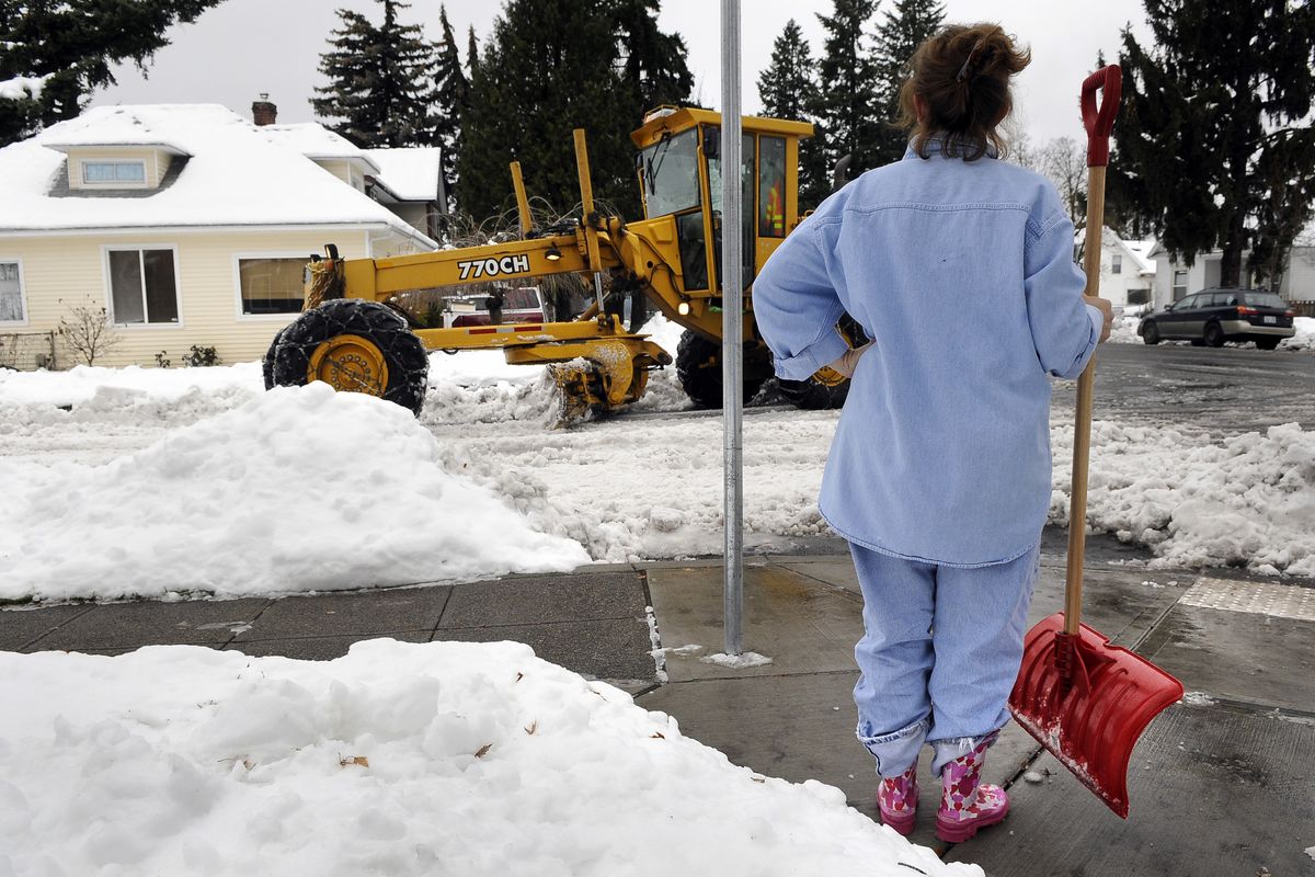 Paula Keith, 51, watches a city snow plow push slush form Indiana Avenue onto Oak Street on Thursday, Dec. 2, 2010.  Keith was trying to clean up the sidewalks at her mother's home on the corner. (Dan Pelle / The Spokesman-Review)
