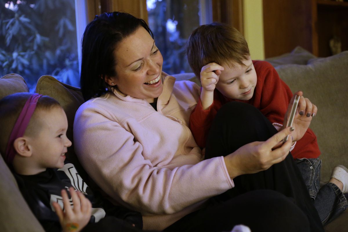 Julie Young relaxes with her sons Nolan, 3, left, and Jameson, 4, while looking at a smartphone in their Boston home on Jan. 27. (Associated Press)