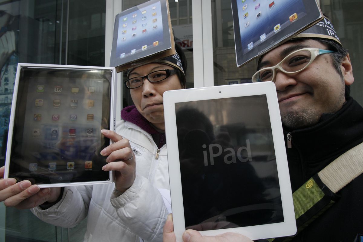 Hisanori Kogure, left, and Ryota Musha show off iPad tablet computers they purchased in Tokyo on Friday. (Associated Press)